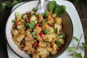 Delicious potato salad garnished with fresh mint, coriander, and pomegranate seeds in a bowl.