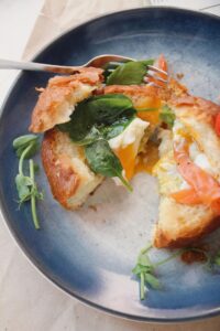 Mouth-watering breakfast sandwich with egg, spinach, and salmon on a plate.